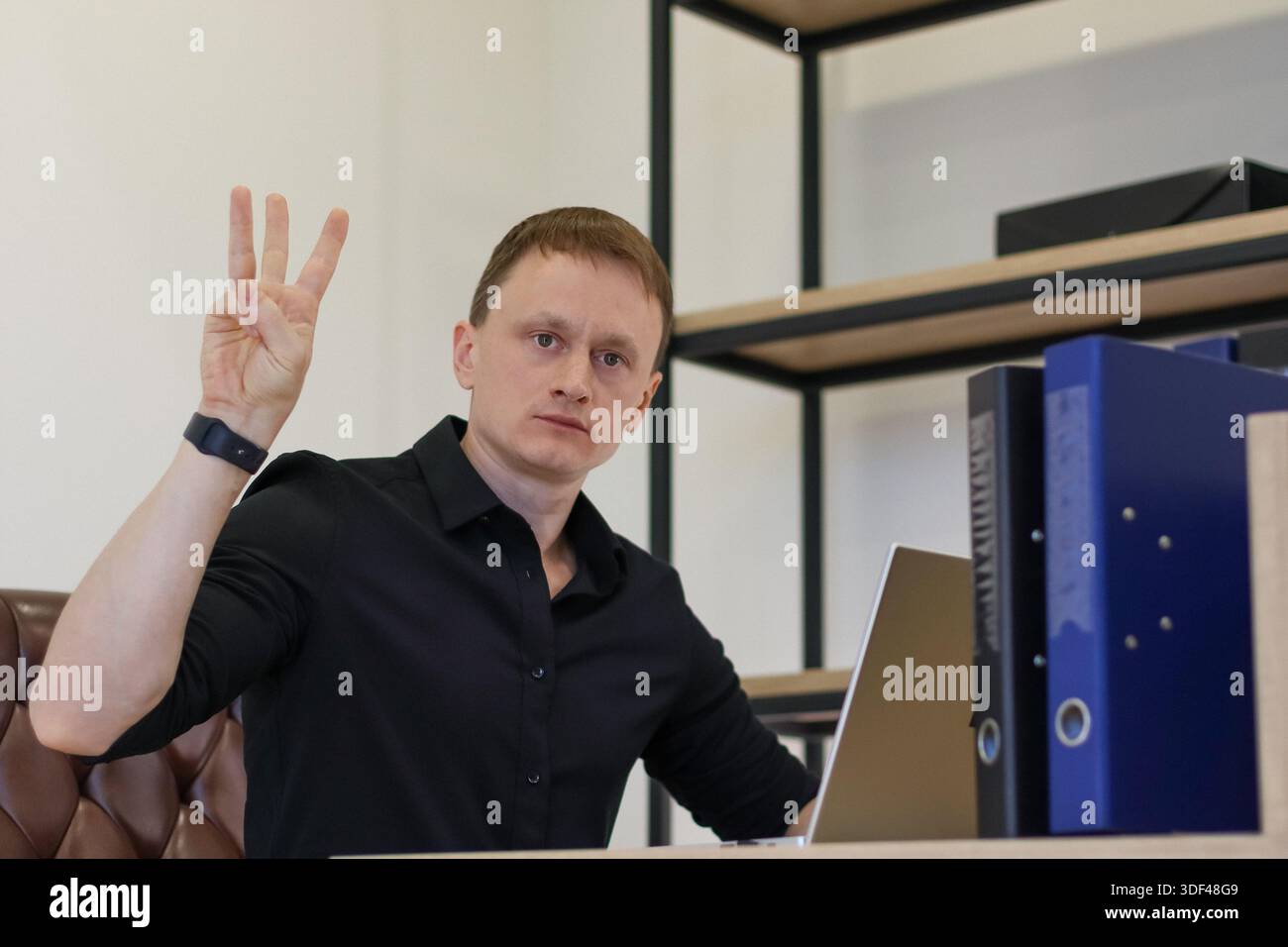 Office worker showing three fingers gesture at desk with computer and document holders Stock Photo