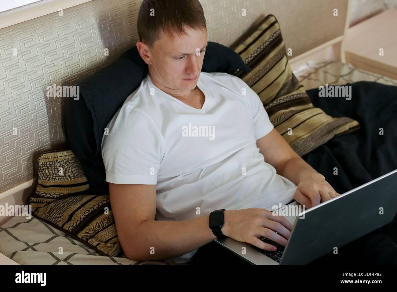 Relaxed male using portable computer for tasks while reclining on bed ...
