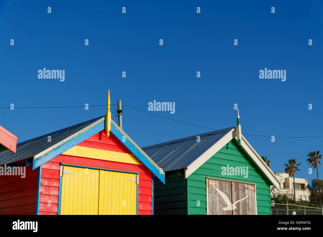Two vibrant beach boxes, one red and yellow striped, the other green with a stenciled seagull, under a clear blue sky. Stock Photo