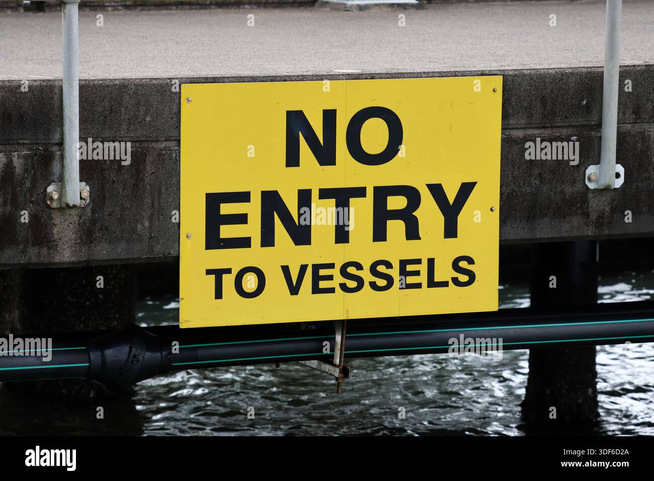 Yellow No Entry To Vessels sign attached to a concrete dock pier at a ...