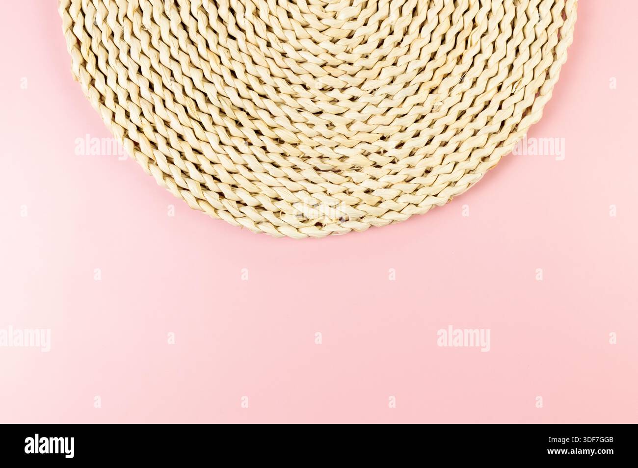 Top view of brown wicker table mat on pink background. Straw round tray, flat lay, copy space. Stock Photo