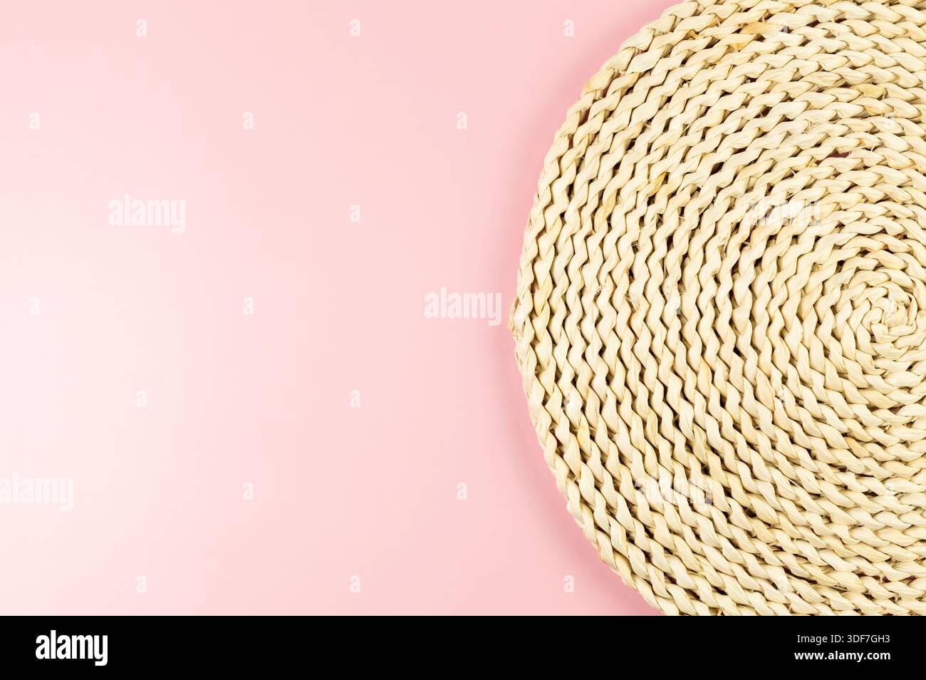 Top view of brown wicker table mat on pink background. Straw round tray, flat lay, copy space. Stock Photo