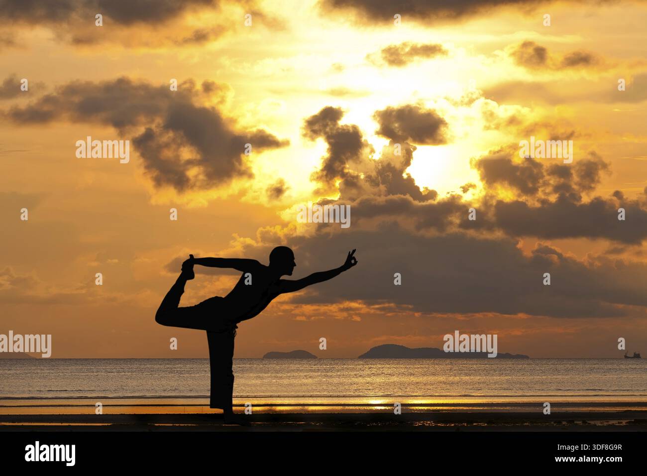 Man silhouette doing yoga exercise natarja at sunset beach Stock Photo