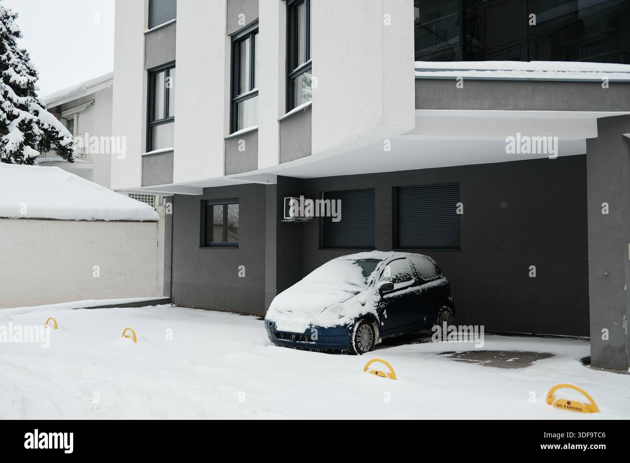 Snow covered car parked beside a modern residential building in winter ...