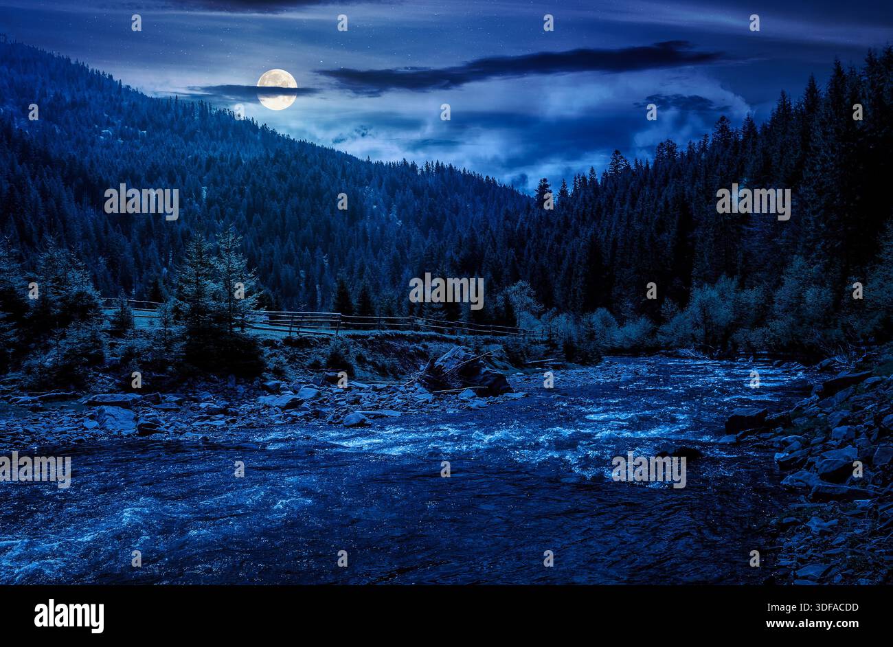 river flows among green forest at the foot of the mountain at night. picturesque nature of rural area in full moon light. serene springtime scenery. b Stock Photo