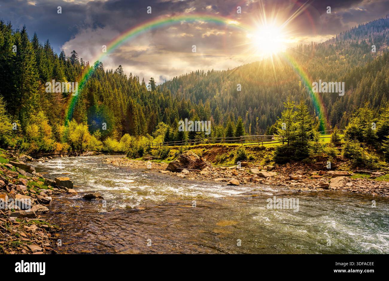 river flows among green forest at the foot of the mountain at sunset. picturesque nature of rural area in evening light. serene springtime scenery. le Stock Photo