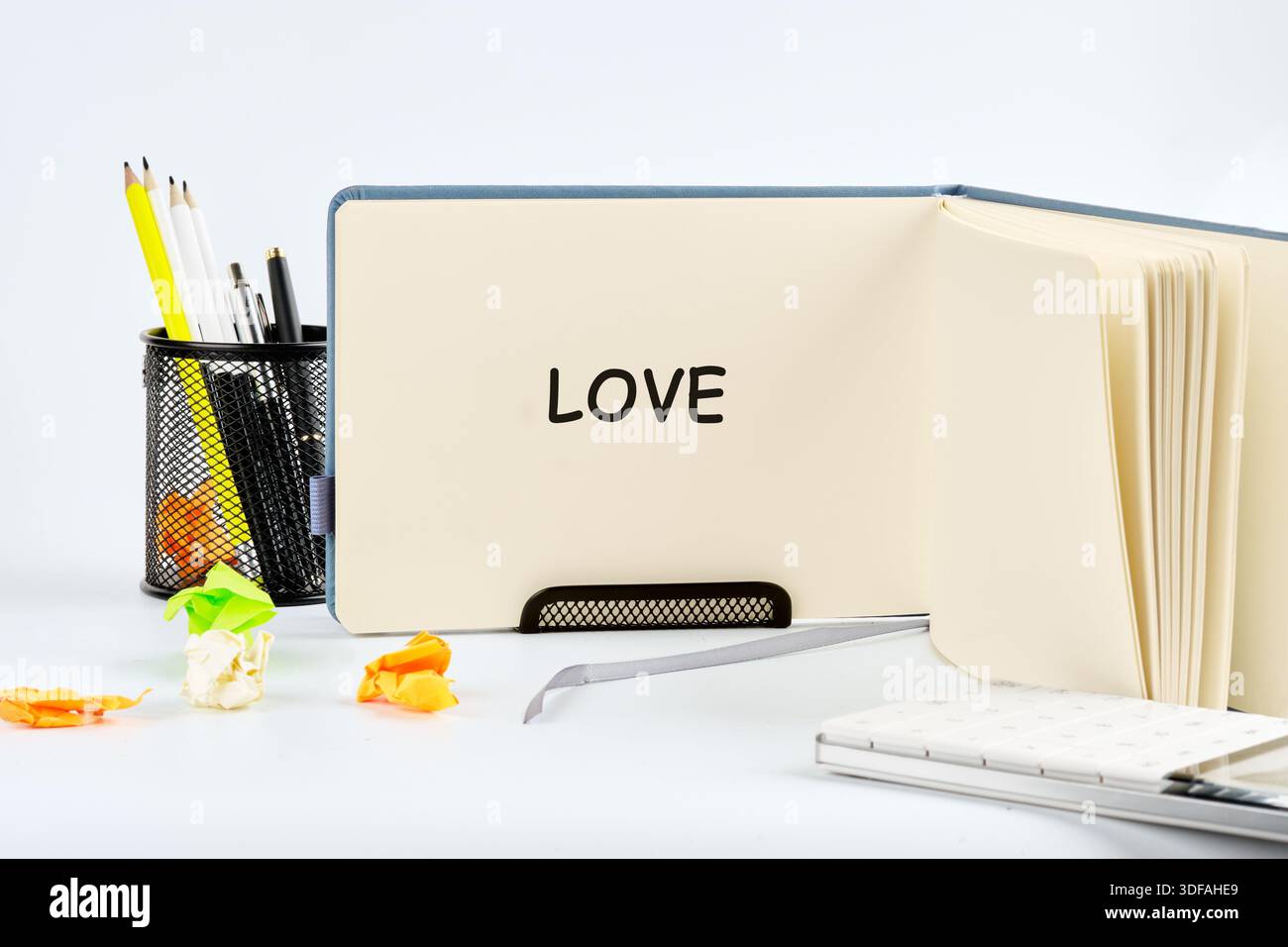 An open notebook displays the word Love. The scene includes pens, pencils, paper scraps, and a delightful mood in a studio, creating a creative and ar Stock Photo