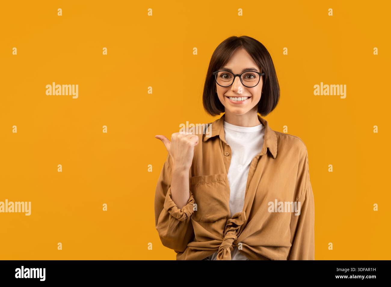 Check this offer. Positive young woman pointing thumb finger aside at free space, advertising your text or design Stock Photo