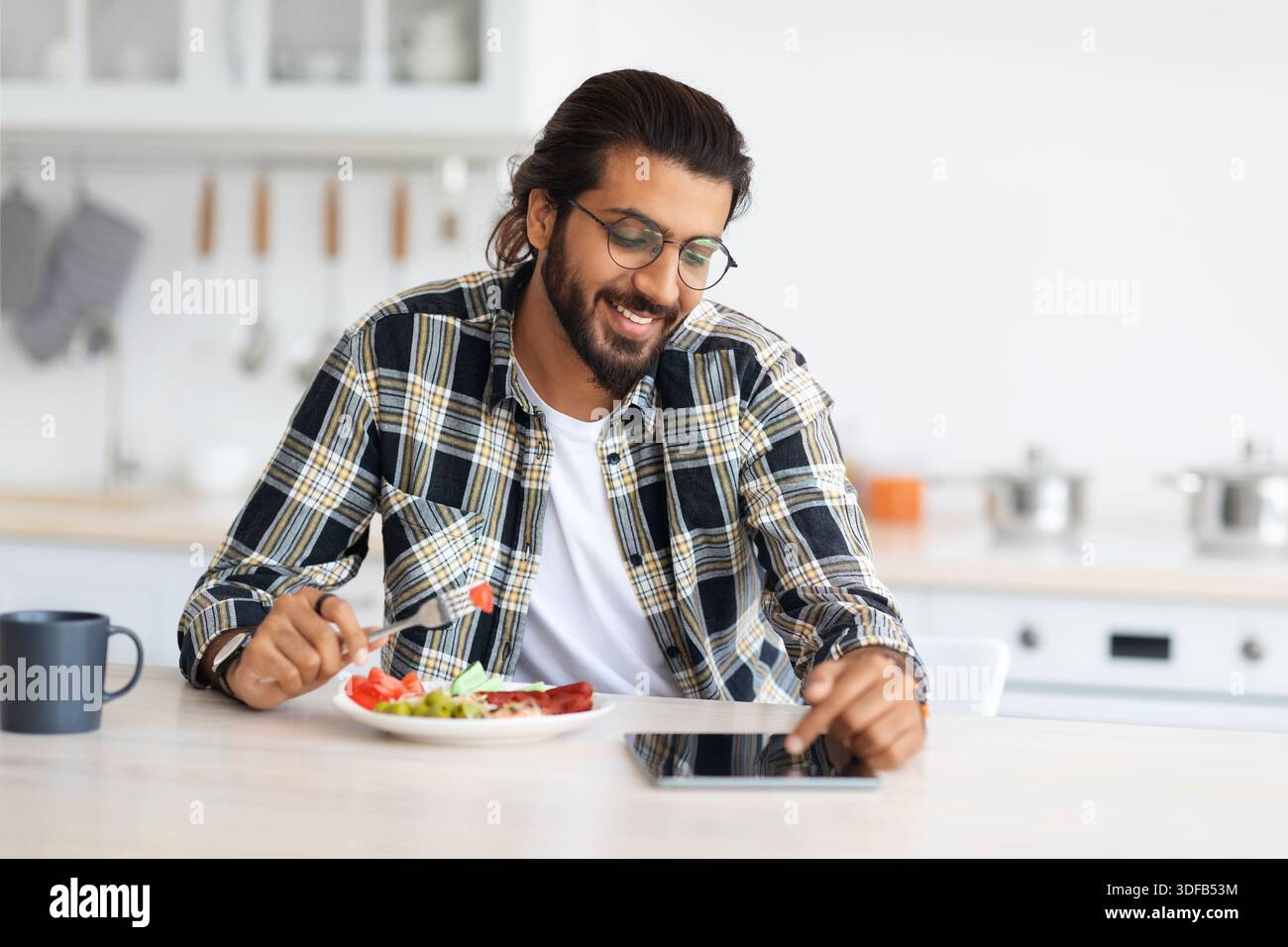 Positive arab guy having breakfast, using digital tablet, copy space Stock Photo