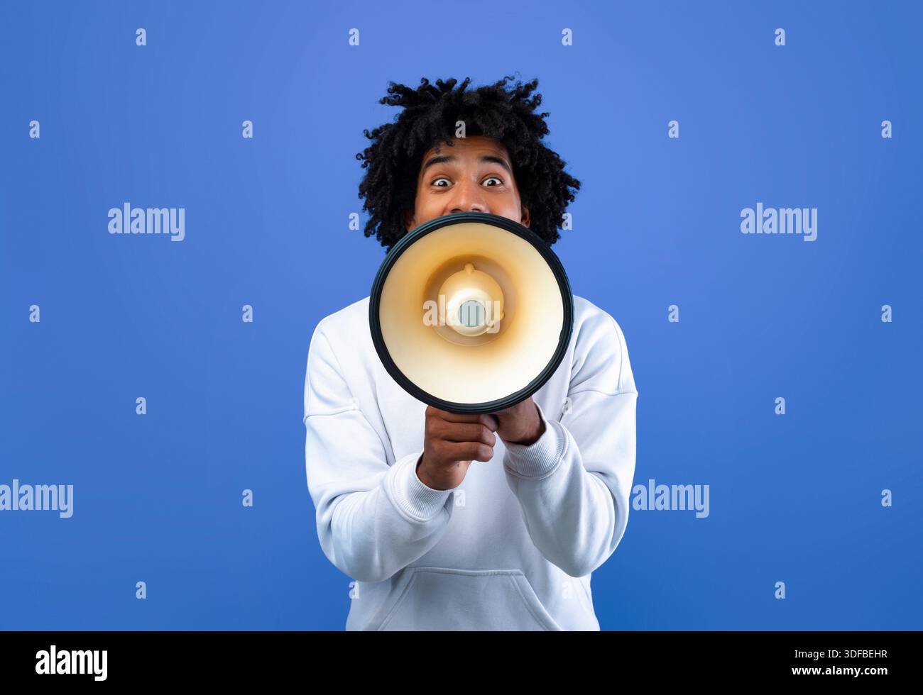 Emotional black teenager making announcement with megaphone on blue studio background Stock Photo