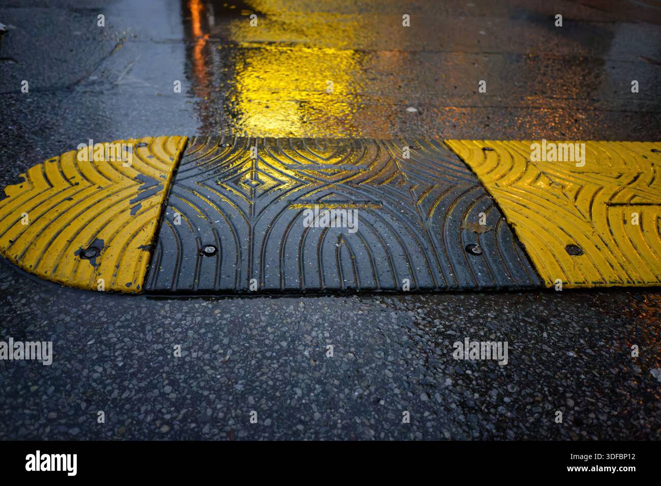 Close-up of a textured yellow and black speed bump on a rainy street ...