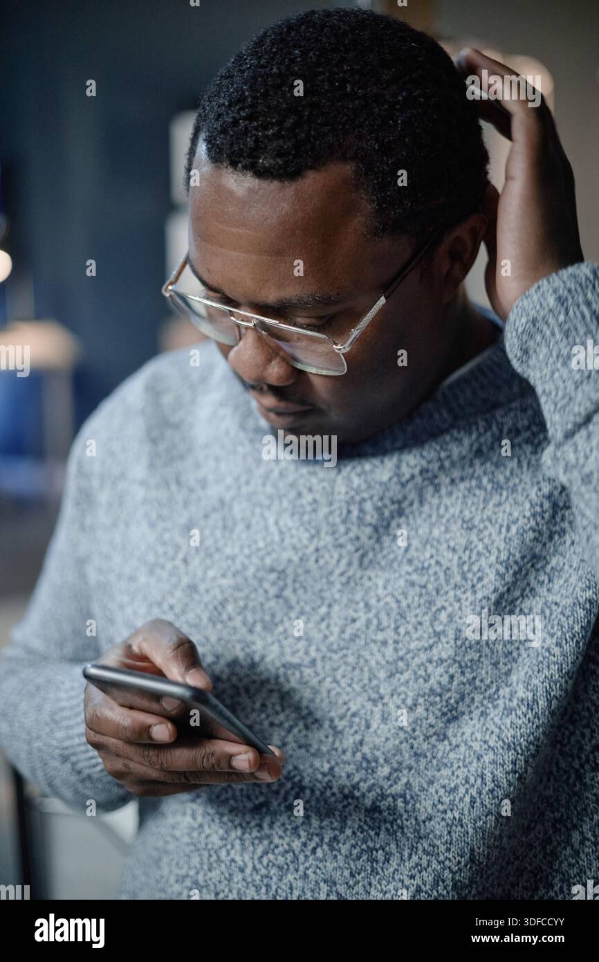 Middle Aged Black Man Using Smartphone While Scratching Head Indoors Stock Photo