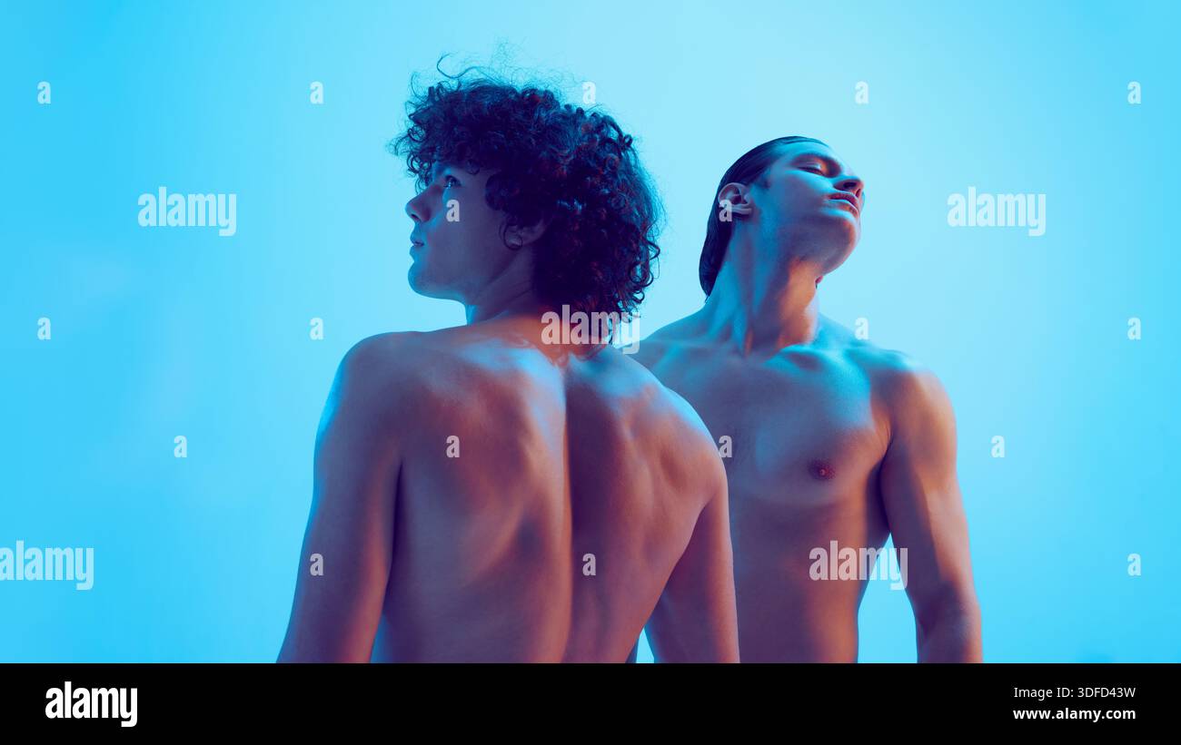 Two young men back view looking upward in blue studio light. Stock Photo