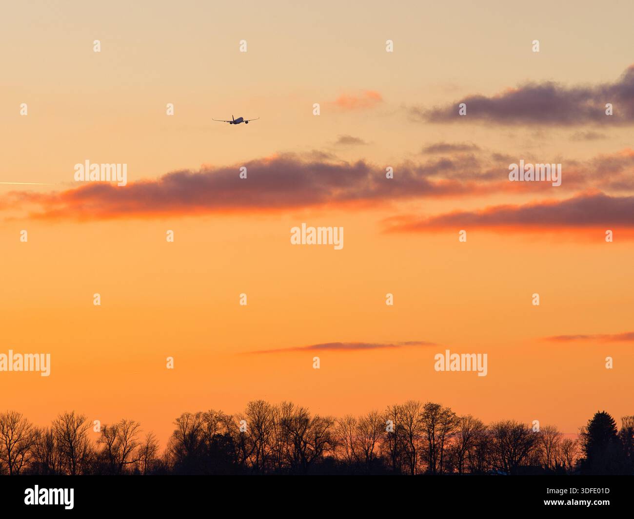Airplane flying through dramatic orange sunset sky Stock Photo