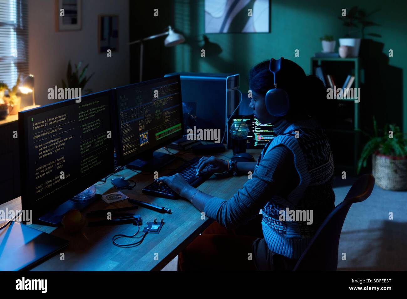 Young Woman Coding Software on Multiple Computer Monitors at Night Stock Photo