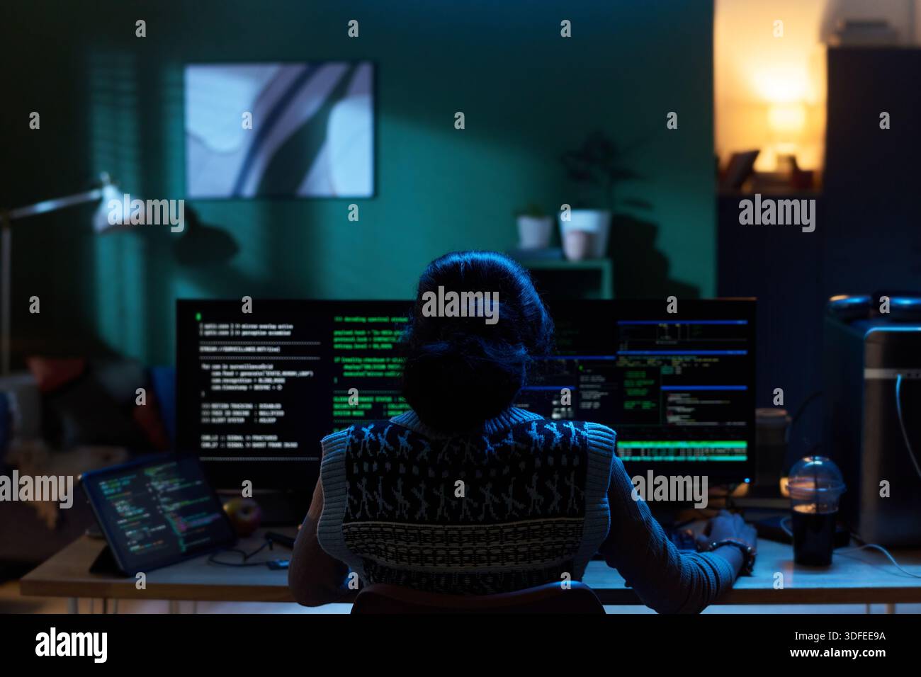 Young Woman Coding on Computer Monitors in Dark Home Office Setting Stock Photo