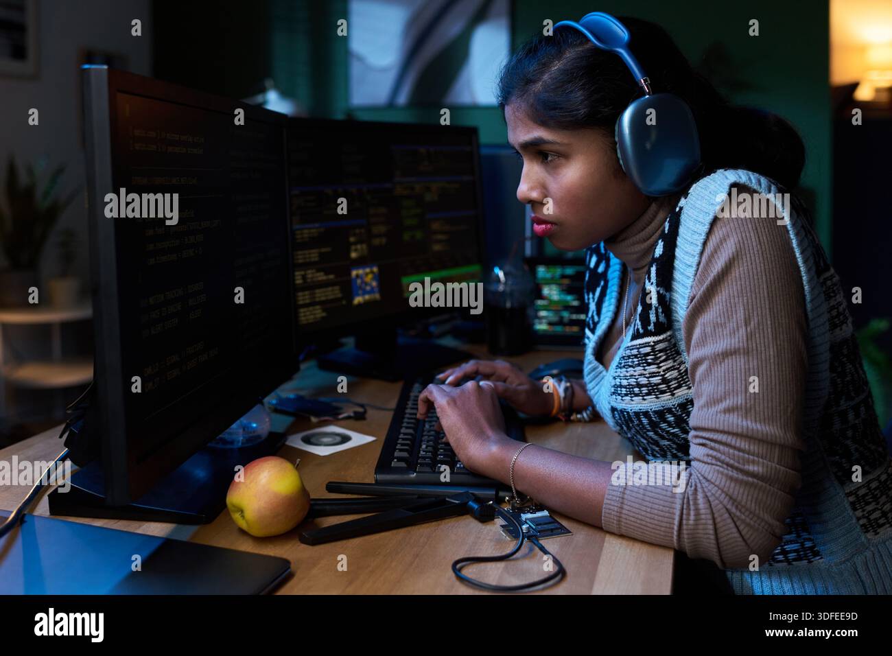 Young South Asian Woman Coding on Computer While Wearing Headphones Stock Photo