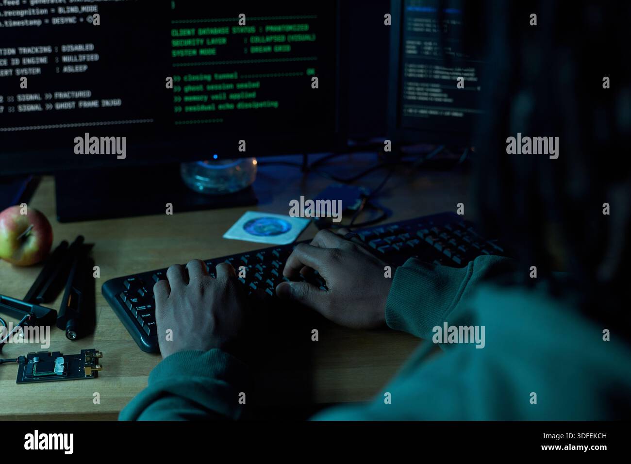Young Black Man Typing Code on Computer Keyboard in Dark Room Stock Photo