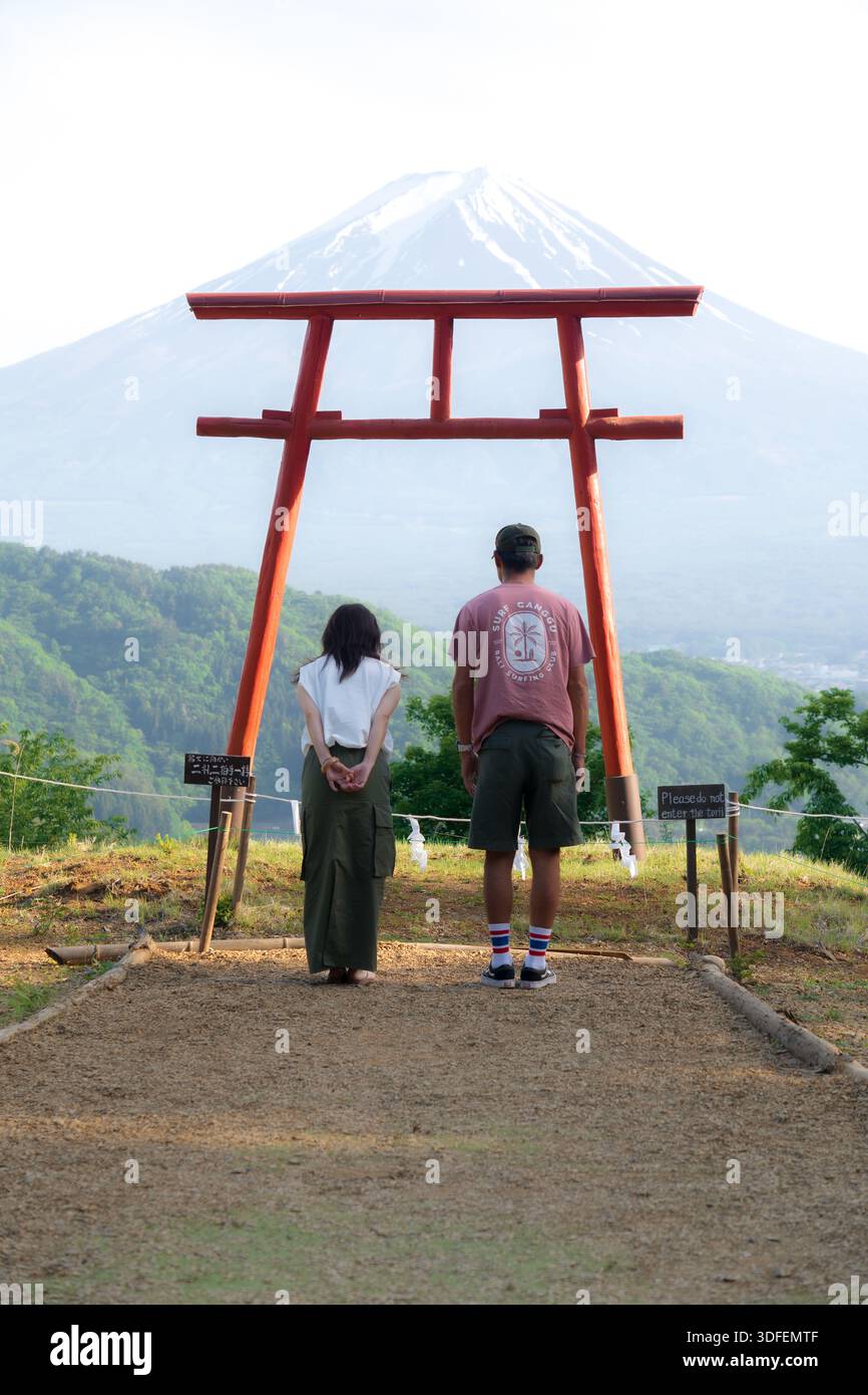 View of a couple standing before a vibrant red torii gate, framing the ...