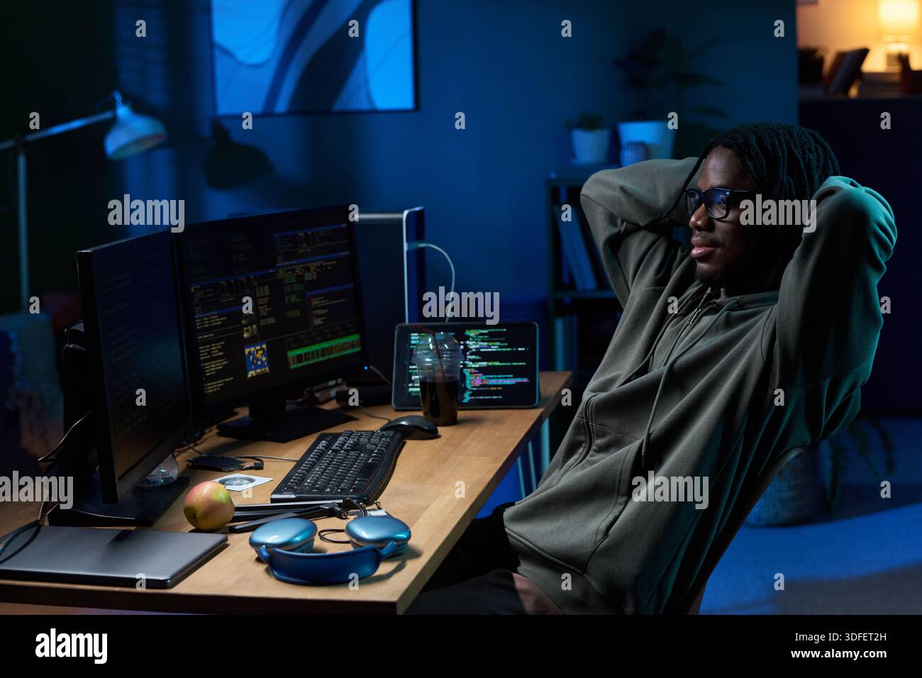 Young Black Man Relaxing While Coding on Computer Monitors at Night Stock Photo