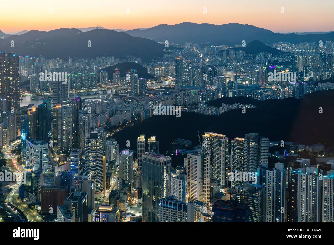 Cityscape of Busan featuring dense high-rise residential buildings, illuminated streets, and surrounding hills at dusk, Busan, South Korea. Stock Photo