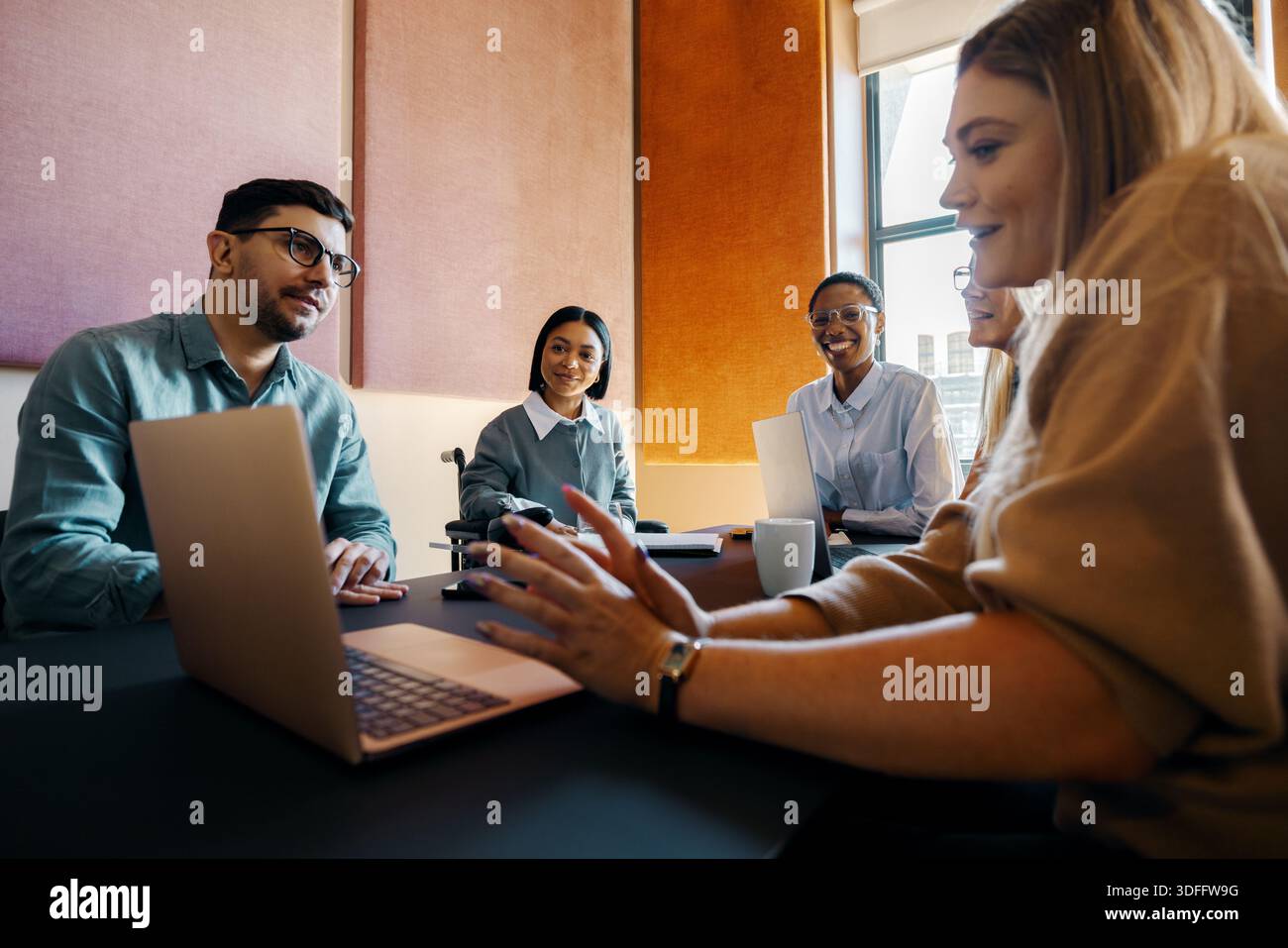 A group of professionals collaborating in a modern meeting room with laptops and documents, fostering teamwork and productivity in a vibrant and diver Stock Photo