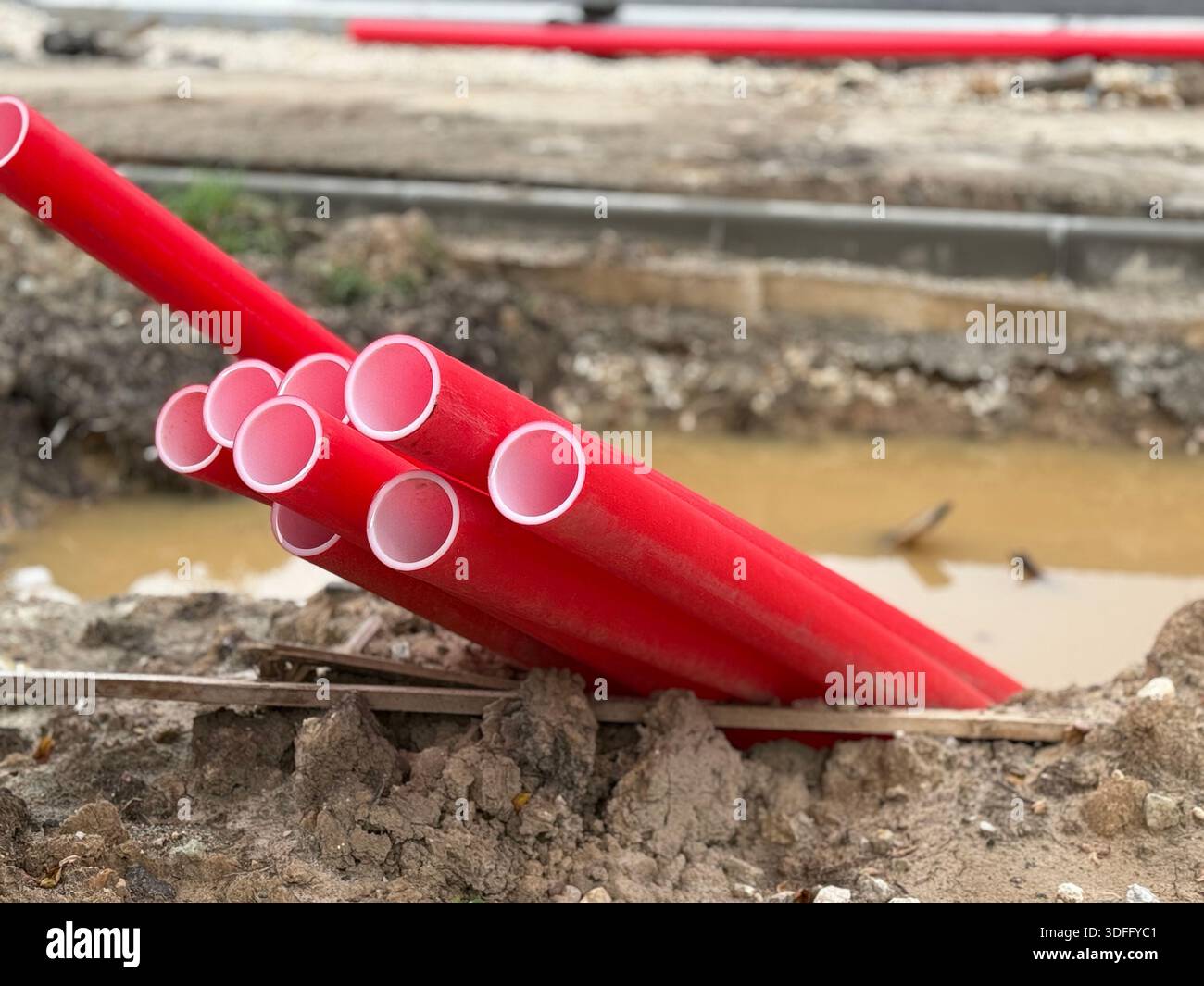 Red PVC pipes stacked on construction site by muddy trench, showcasing ...