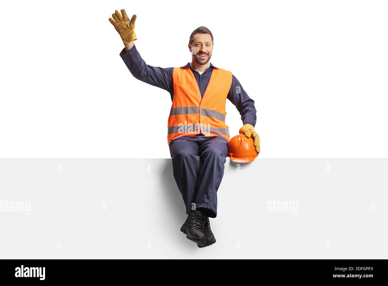 Smiling construction worker sitting on a panel and waving isolated on white background Stock Photo