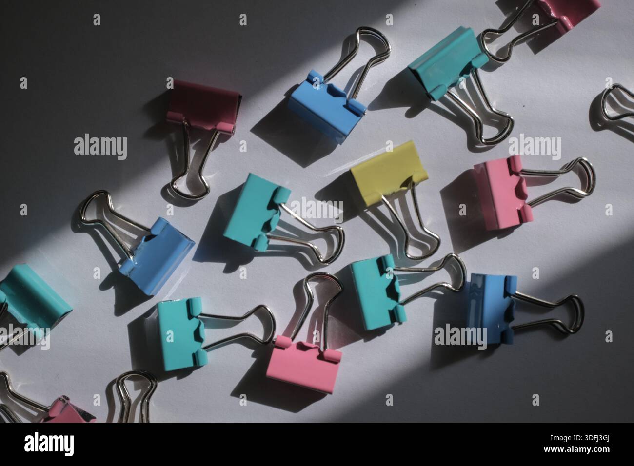 Colorful binder clips scattered on a surface with shadows Stock Photo