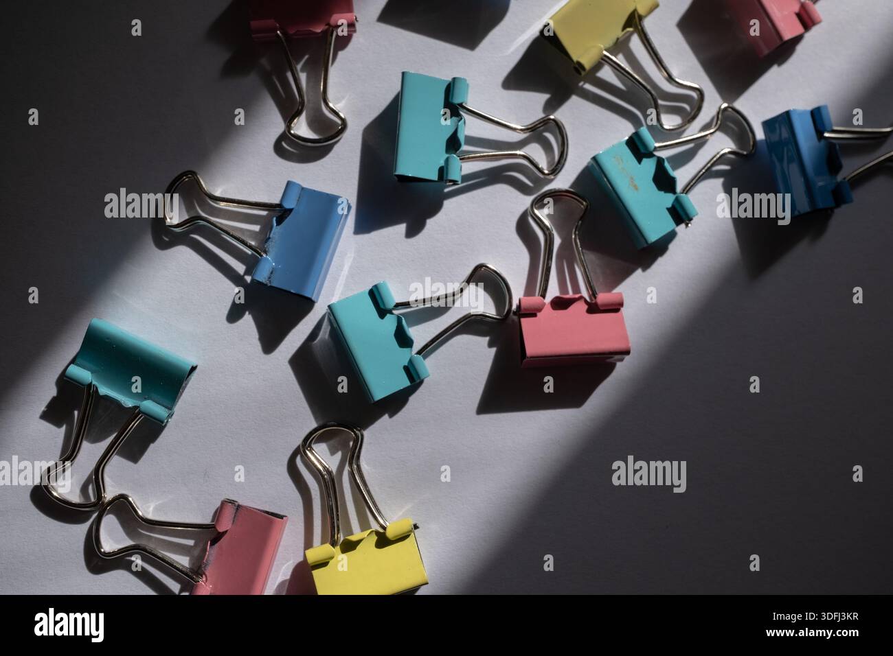 Colorful binder clips scattered on a surface with shadows Stock Photo