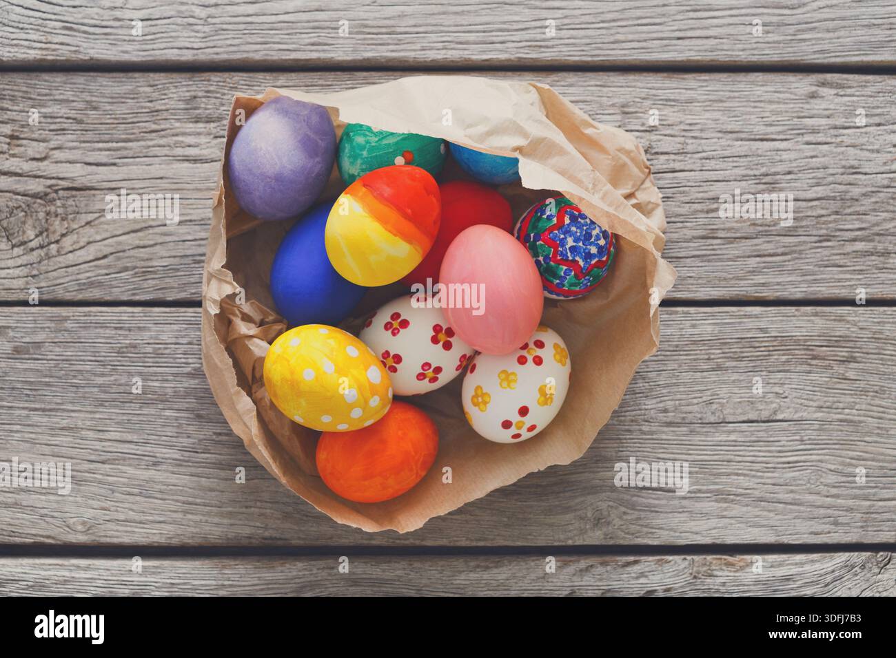 Brightly Colored Easter Eggs Arranged in a Crumpled Paper Bowl on a Wooden Table Stock Photo