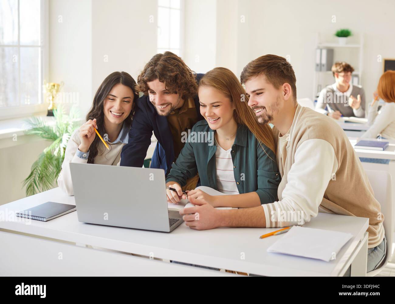 Happy university students collaborating on task, using laptop and preparing project or presentation. Stock Photo