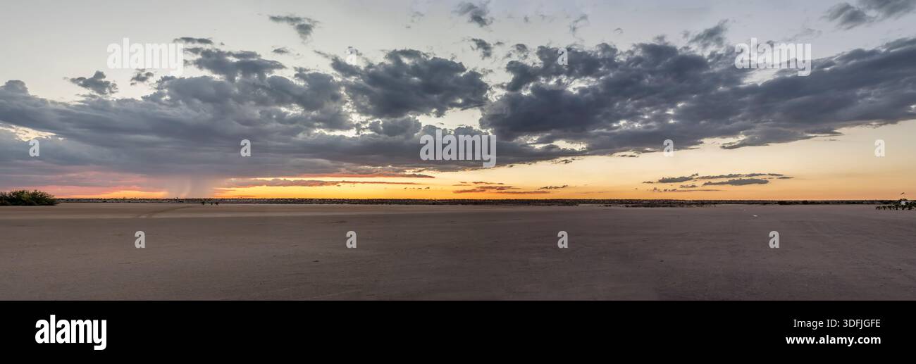 landscape with rain showers and clouds in red sky over pan airfield at sunset, shot in bright late spring light at Bitterwasser, Hardap, Namibia Stock Photo