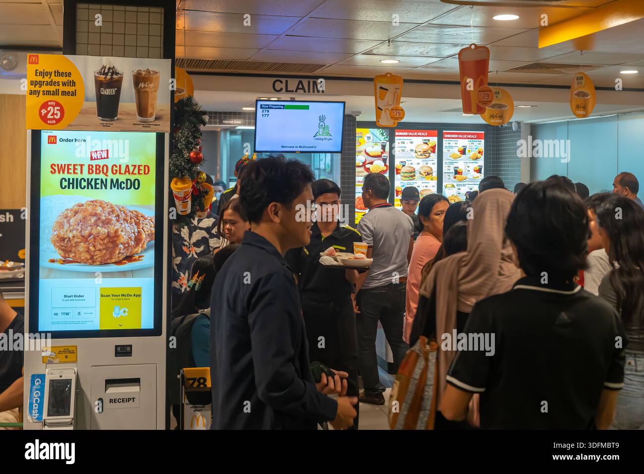 interior of a busy McDonald's restaurant, self-service ordering kiosk advertising a new "Sweet BBQ Glazed Chicken McDo", long queue of customers. Cebu Stock Photo