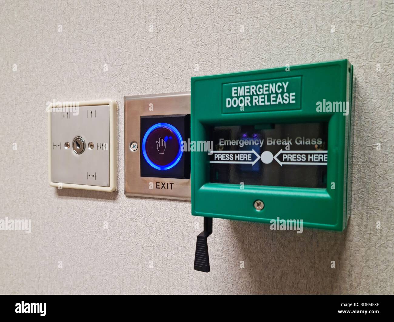 Multiple building access control devices mounted on a textured interior wall. Components include a key switch for security override, a sensor-based to Stock Photo
