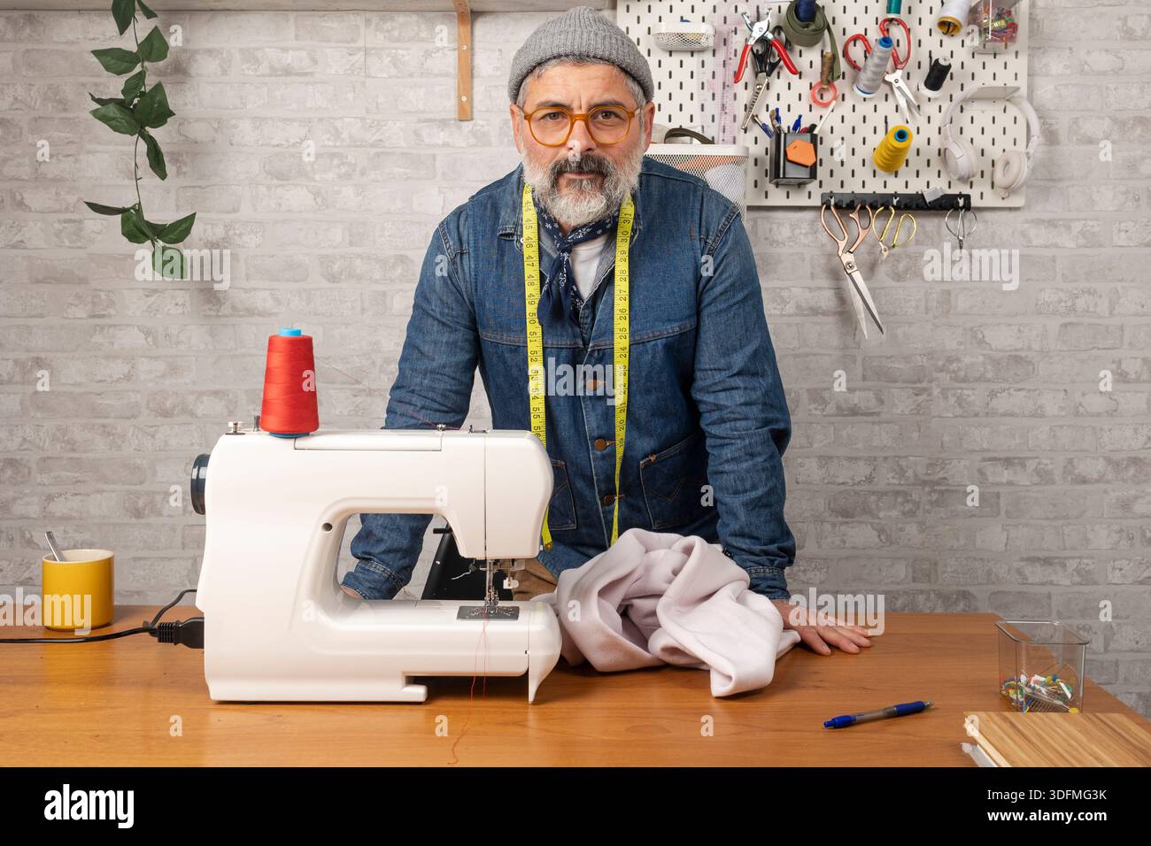 Male fashion designer working in his workshop with a sewing machine and fabric Stock Photo
