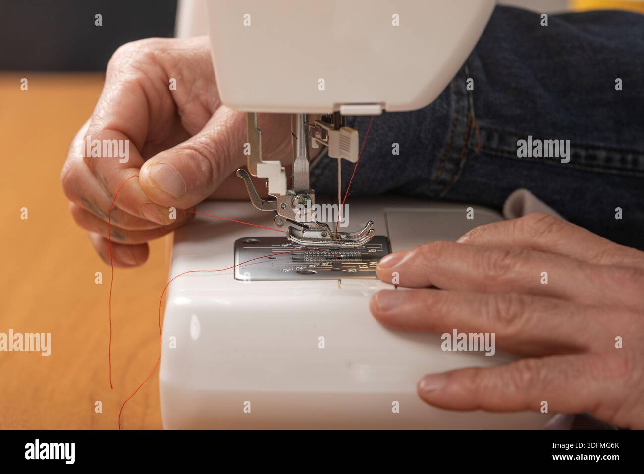 Hands threading red yarn into a sewing machine, preparing for sewing Stock Photo