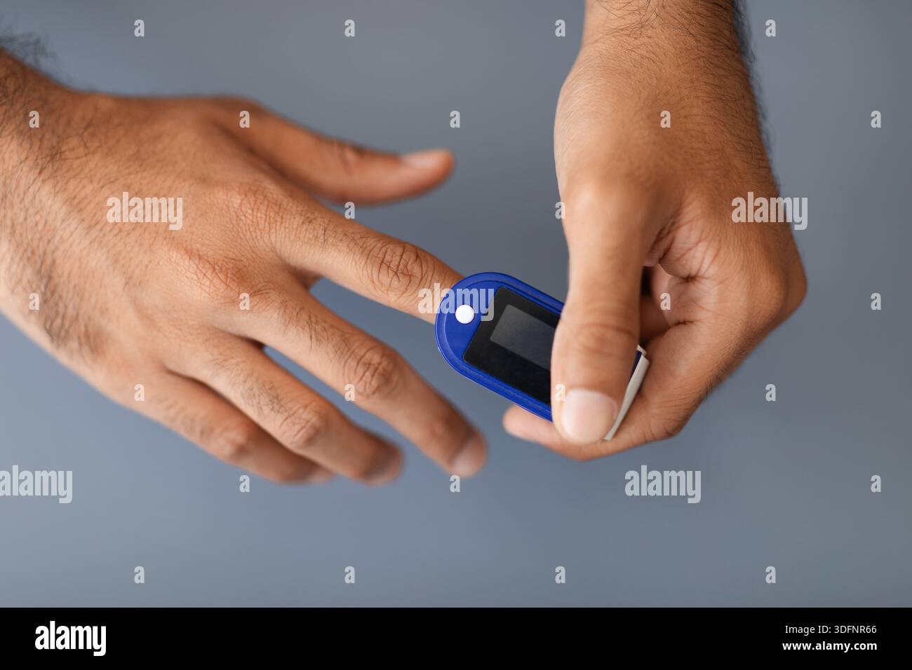 Unrecognizable man using pulse oximeter, grey background Stock Photo