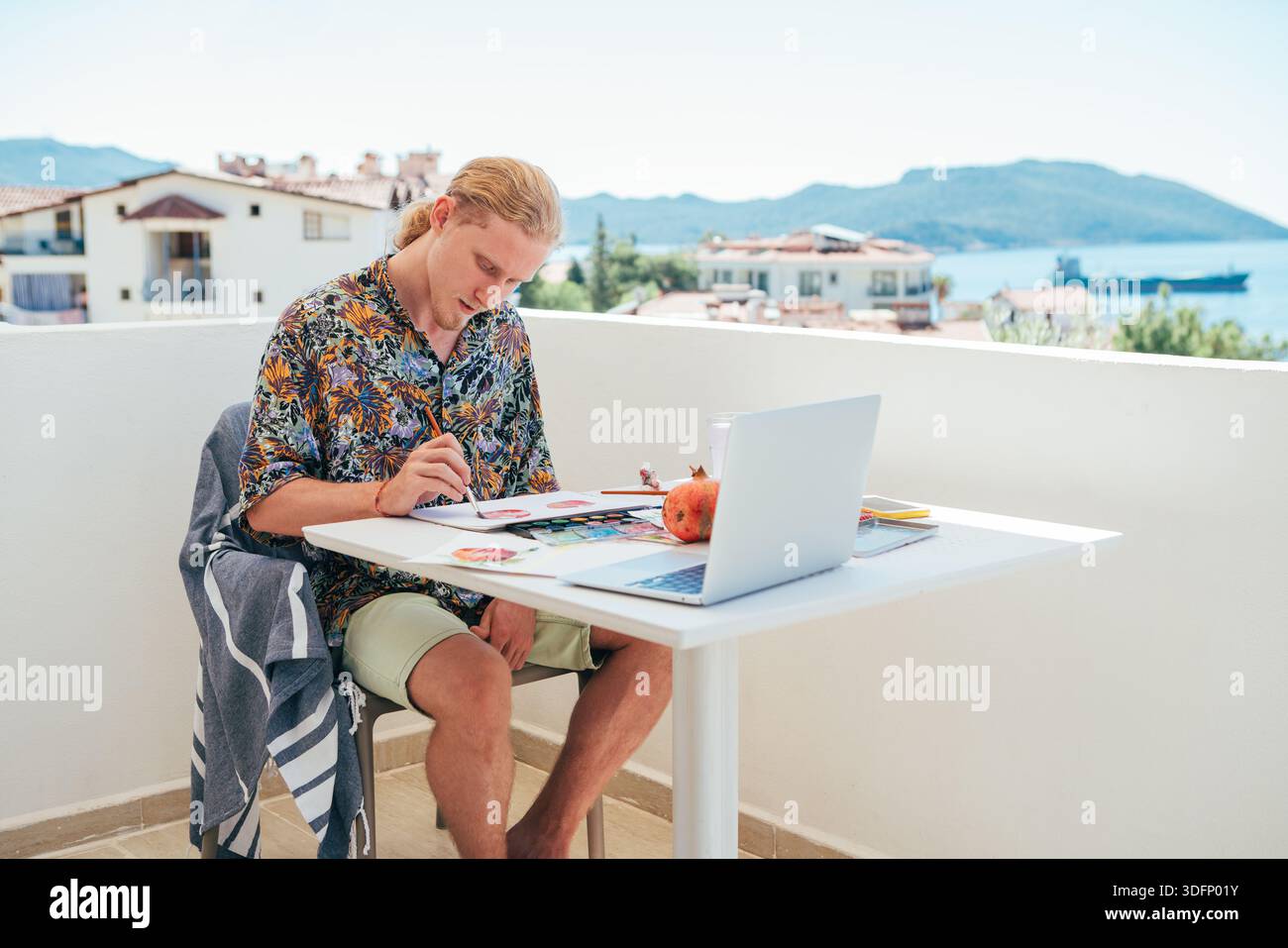 Teenager boy painter sitting balcony creating watercolor artwork seaside summer vacation. Enjoying creative process sunny coastal atmosphere combining Stock Photo