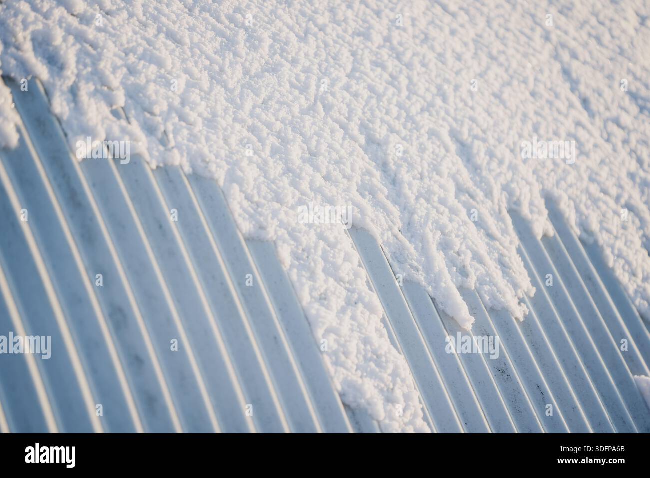 Snow layer on corrugated steel roofing sheet, close view of ridges and ...