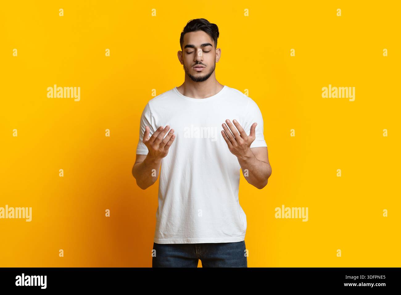 Young arab man praying for luck on yellow Stock Photo