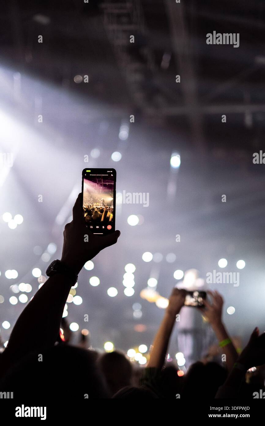 Hand holding a smartphone recording a concert, with bright stage beam ...
