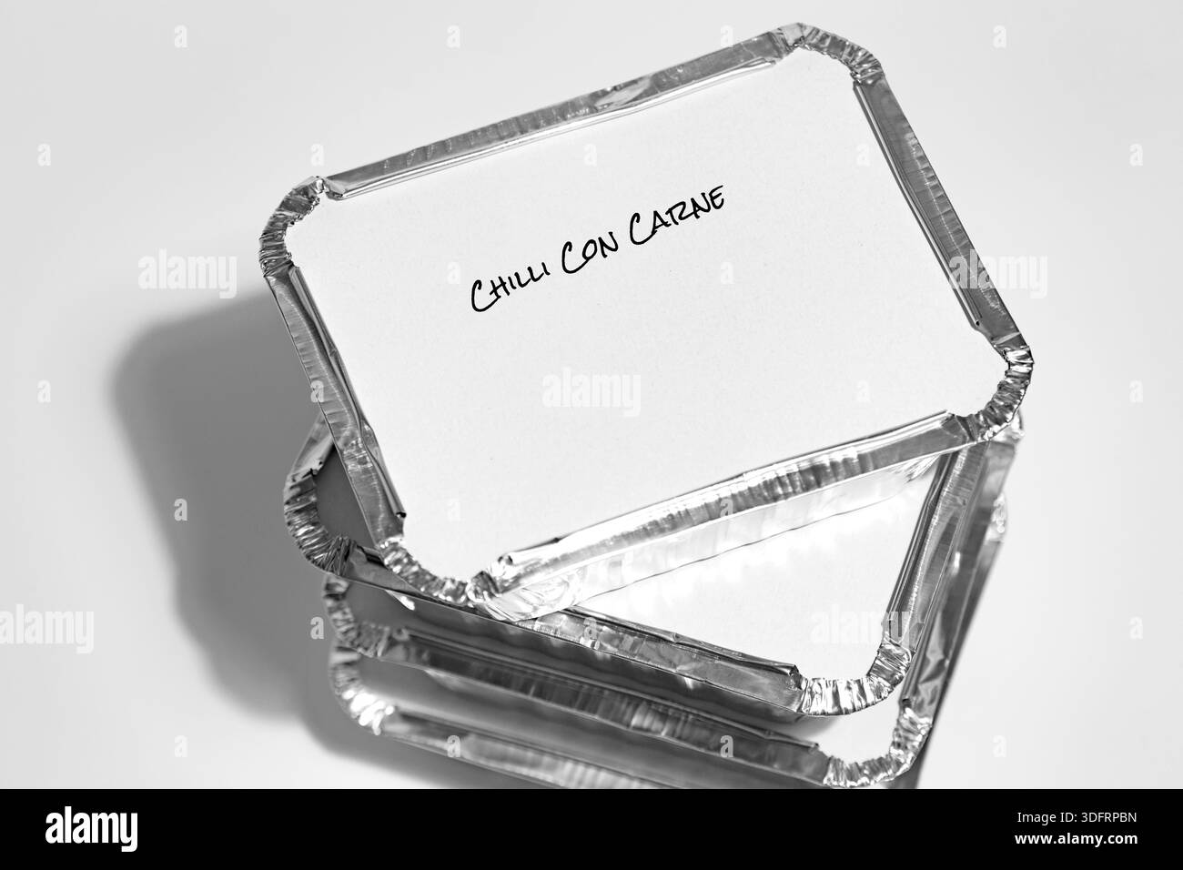 Individual foil tray containers filled with homemade chilli con carne ready for freezing. Ideas for cutting the cost of food. Stock Photo