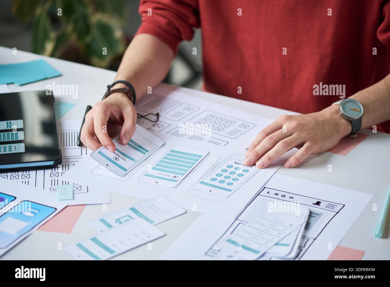 Unknown man working on mobile app interface design, arranging paper prototypes and wireframes on desk, using hands to organize layout and plan user experience Stock Photo