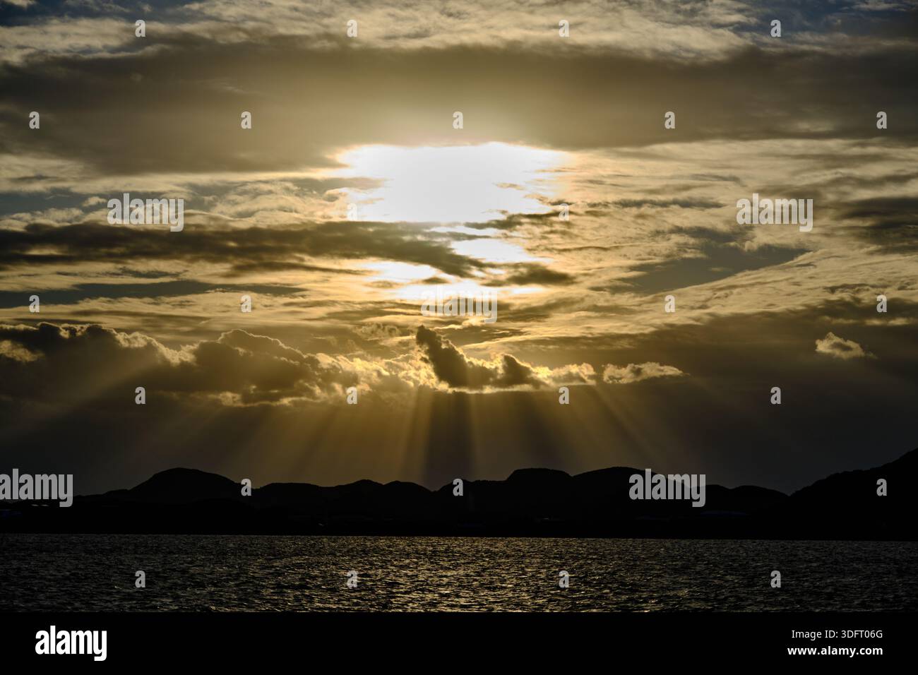 A breathtaking, high-contrast image capturing dramatic crepuscular sun rays bursting through a dense layer of dark, moody clouds. Stock Photo