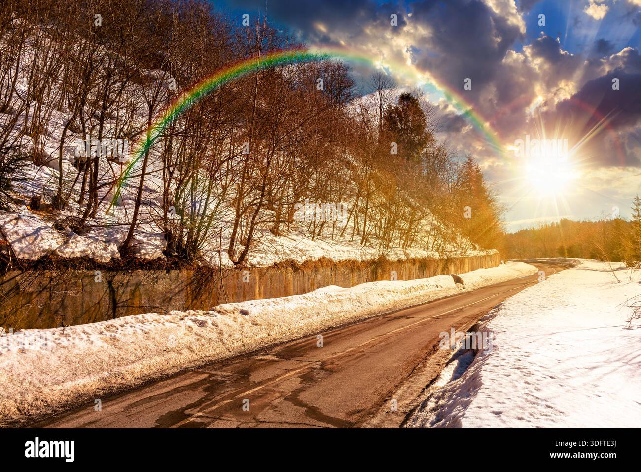 country road winding through winter landscape under blue sky at sunset. mountains in evening light. travel background with snow covered slopes. storyt Stock Photo
