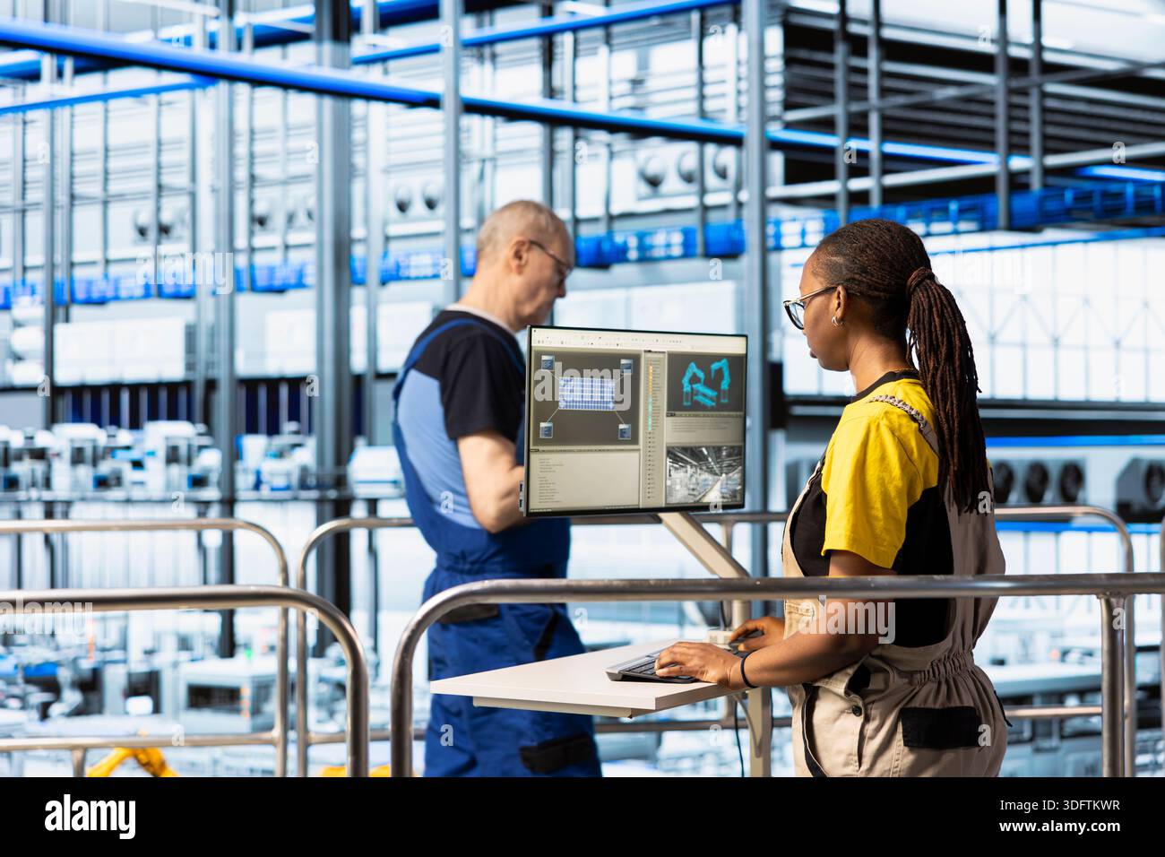 Factory worker operating control panel on elevated platform overlooking automated production line. Female engineer managing industrial machinery workflow using digital interface Stock Photo