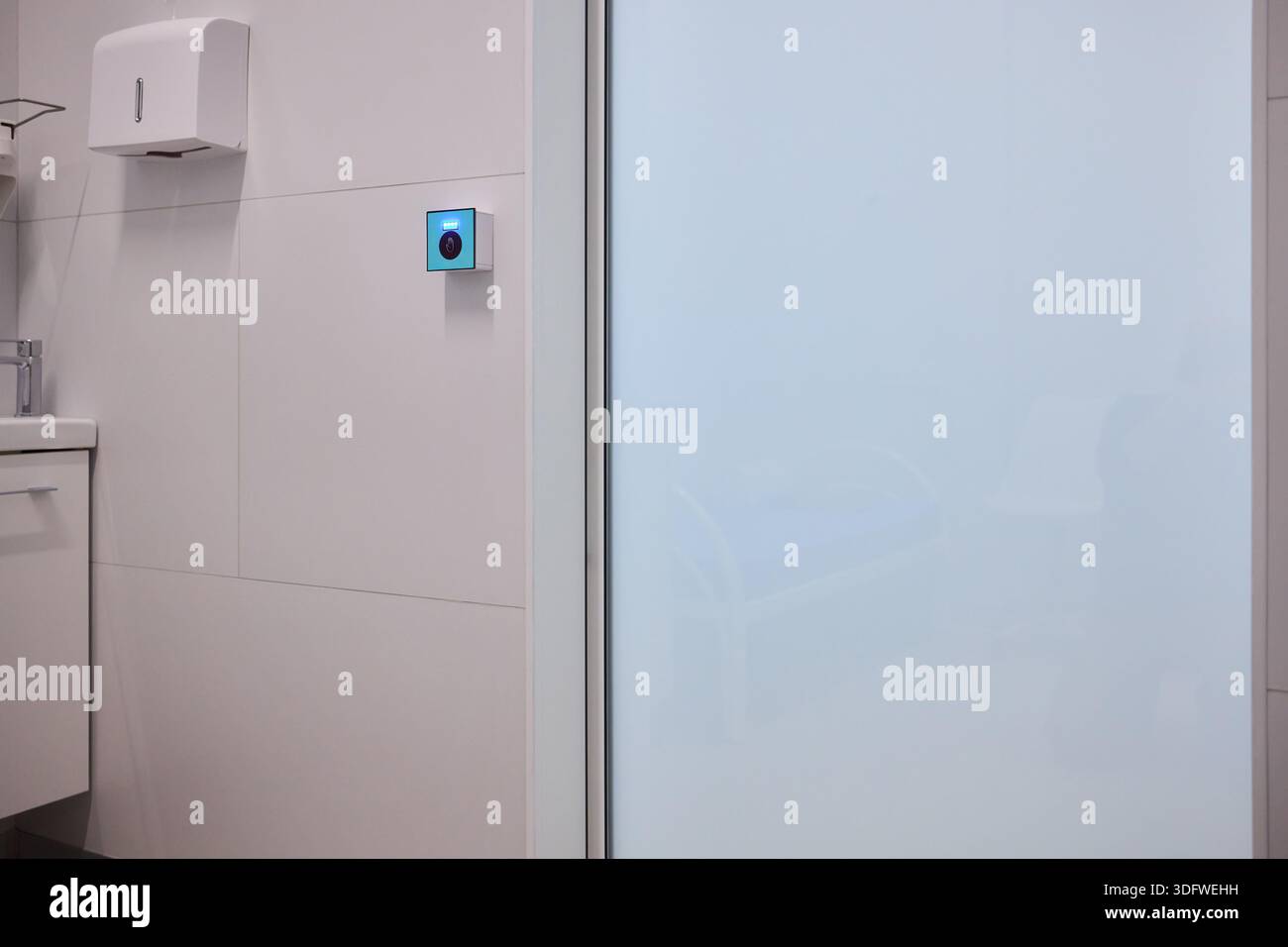 This is a modern smart touch sensor device installed on a wall, featuring a blue LED indicator Stock Photo