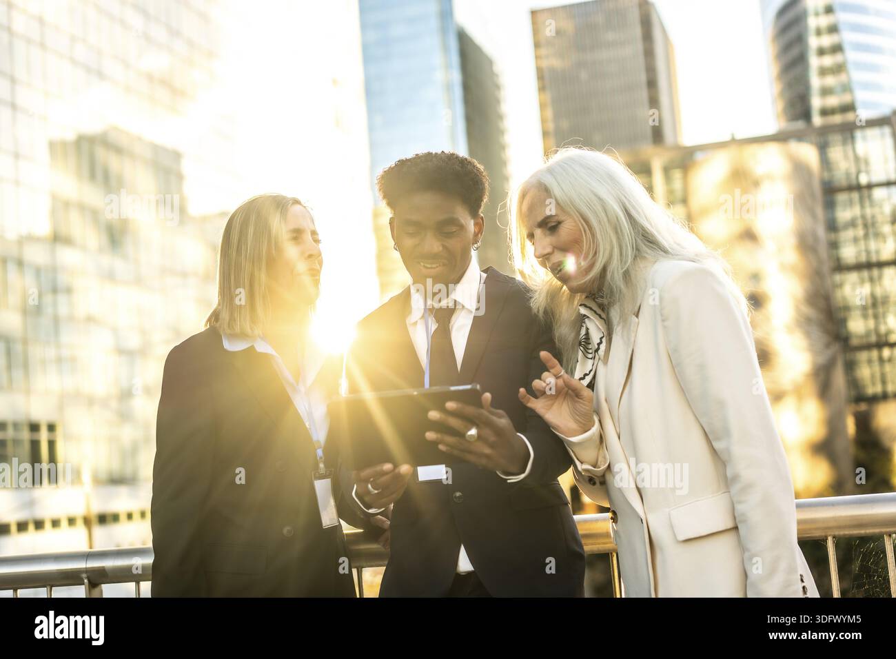 Diverse multi generation business team outdoors at sunset, collaborating over a digital tablet amid urban skyscrapers teamwork, technology and leaders Stock Photo
