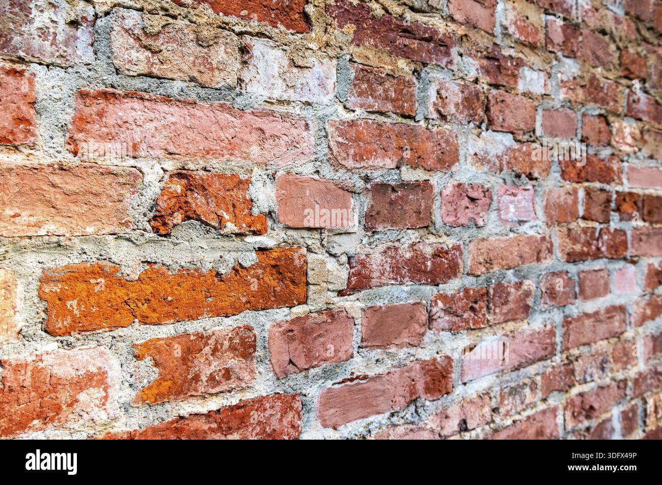 Rough red brick wall as background texture. Bricks masonry with uneven seams. View from the angle Stock Photo